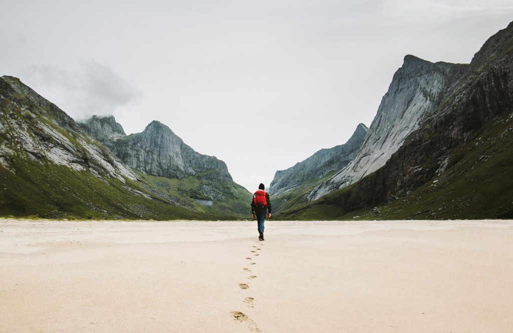 Man walking on deserted beach headed toward mountains